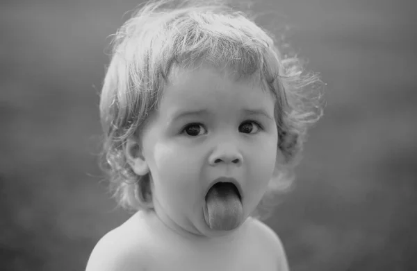 Funny child in park. Baby face with tongue close up. Funny little child closeup portrait. Blonde kid, emotion face
