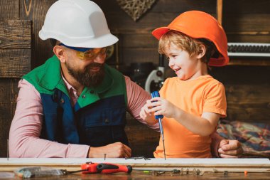 Küçük oğlu inşaatta babasına yardım ediyor. Koruyucu miğferli ebeveyn küçük oğluna okulda farklı aletler kullanmayı öğretiyor.