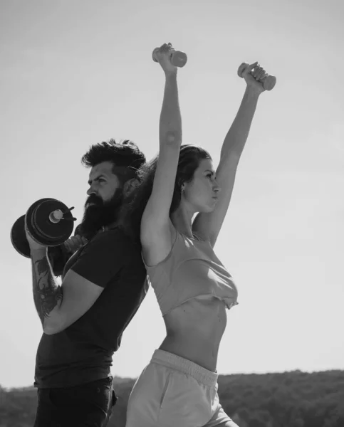 穿着性感粉色运动服的胖女人 强壮的健身夫妇 留着胡子的男人和性感的女人在户外锻炼 精力充沛的夫妇带着哑铃进行训练 在室外进行肌肉运动 — 图库照片