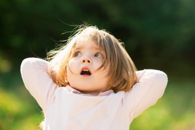 Baharda yeşil çimlerde gezen süpriz kız çocuğu. Parkta yürüyen küçük çocuklar. Duygusal bebek yüzü
