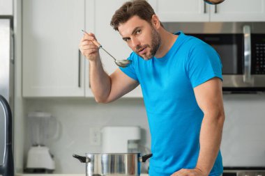 Aşçı adam mutfakta tencerede yemek pişiriyor. Gurme yemeği hazırlama süreci. Adam evde yemek pişiriyor, esrar kullanıyor. Şef yemek pişiriyor. Yakışıklı aşçı aşçı konsepti