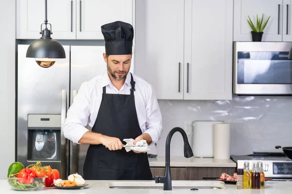 シェフ成熟した男は台所でエプロンを調理します 台所で食べ物を準備するハンサムな男 おいしい食事を作る男 肉や野菜とキッチンの男 ポートレートのカジュアル男でエプロンでキッチン — ストック写真