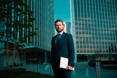 İş adamının elinde dizüstü bilgisayar vardı. İş yerinin yakınında duruyordu.