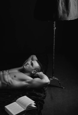 Yatakta kitap okuyan yakışıklı, üstsüz genç adam. Zeki ve zeki gay.