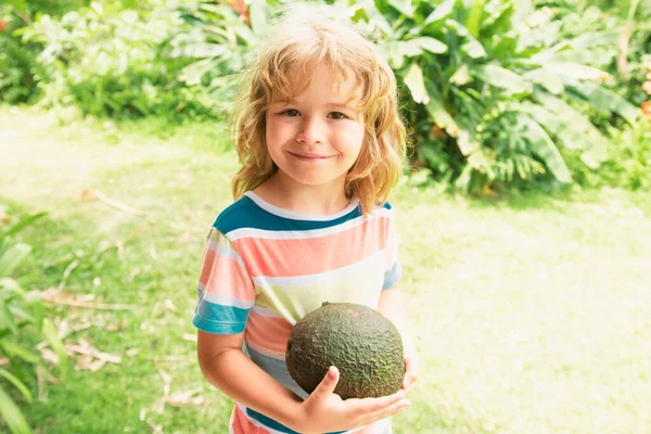 夏の庭でアボカドを見せてくれる幸せな子供 子供の健康食品 — ストック写真