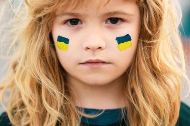 Çocuk yanağında Ukrayna bayrağı işareti var. Ukrayna jeopolitik dünya krizi. Çocuklar yüzünüzü kapatın.