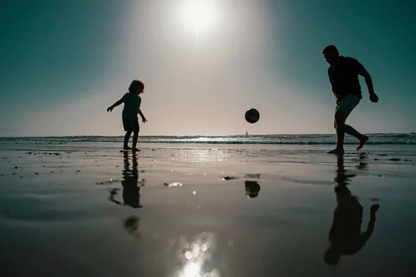夏の日に遊んでいる子供の男の子とお父さん 父と息子は夏休みにビーチでサッカーやサッカーをする — ストック写真