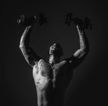 Strong man raising the dumbbells up. Intense workout. Body with tattoo