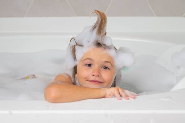 Çocuk şampuanı. Küvette küçük bir çocuk. Banyoda yıkanmak. Saçında sabun köpüğü olan çocuk banyo yapıyor. Gülümseyen çocuk portresi, sağlık sigortası ve çocuk hijyeni. Çocuklar küvette köpükle yüzüyorlar.