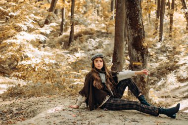 Parkta yürüyen güzel bir kadın ve güzel sonbahar doğasının tadını çıkarıyor. Sonbahar manzarasında genç ve güzel bir bayanın açık hava moda fotoğrafı.