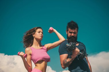 Sporty couple with dumbbell outdoors. Couple working out with dumbbells. Fitness club outside on nature. Fitness sexy models pumping up arm with dumbbell
