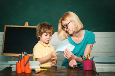 Okula ve eğitim anlayışına geri dönelim. Öğretmen genç çocuğa ders konusunda yardım ediyor. Kitaplı ilkokuldan gelen çocuk