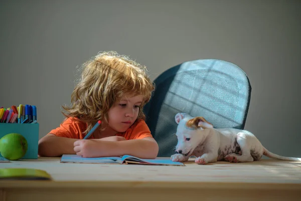 子犬の犬とかわいい男の子は彼女の宿題をする 教育の子供時代と学校のコンセプト 自宅でノートにペットの書き込みでかわいい学生 — ストック写真
