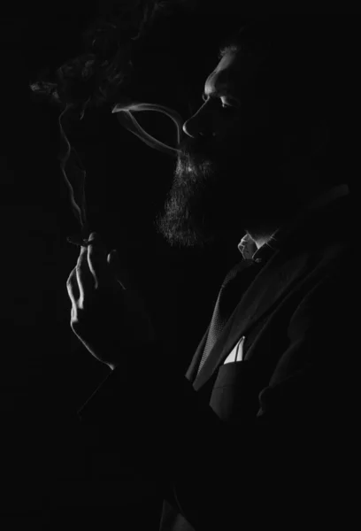 スーツを着たビジネスマンがタバコを吸う 暗い影で顔若い男喫煙上の黒の背景 — ストック写真