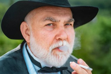 Gri sakallı, sigara içen yakışıklı son sınıf öğrencisinin yüz portresi. Çekici, yaşlı, olgun bir adam. Takım elbiseli, kravatlı ve şapkalı ihtişamlı bir adam. Gangster bak, mafya pezevengi.