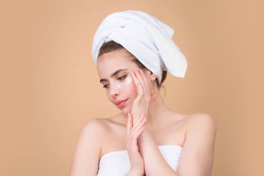 Göz bandı takan bir kadın. Gözlerinin altında kolajen bloknotları olan, gözlerinin etrafındaki hassas cilde dikkat eden bir kızın portresi. Kadın yenilenme cilt bakımını yamalıyor