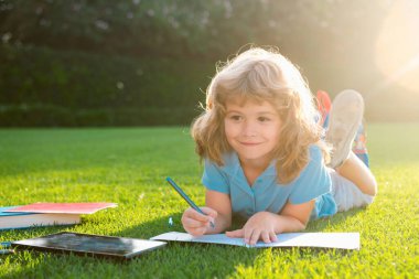 Açık havada kitapçığa notlar yazan sevimli çocuk. Okul rüyası. Hayalperest okul çocuğu. Hayaller ve hayal gücü. Hayalci okul çocuğu suratı.