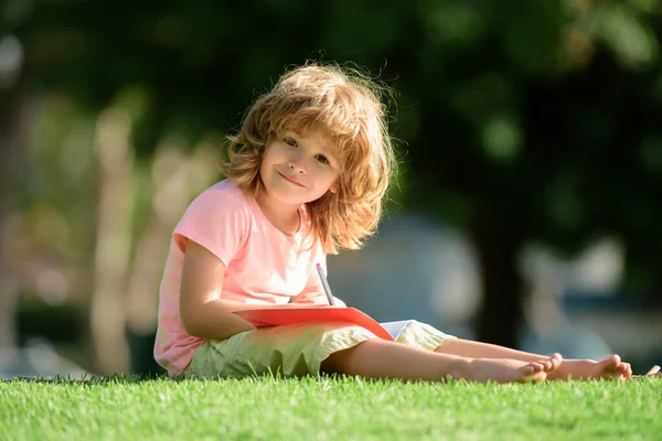 Lächelnder Schüler Vorschulalter Der Park Auf Gras Ein Notizbuch Schreibt — Stockfoto