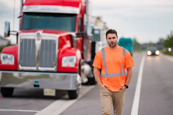 Men driver near lorry truck. Truck driver in safety vest satisfied near truck. Hispanic trucker. Trucking owner. Transportation vehicles. Handsome man posing in front of truck. Semi trucks vehicle