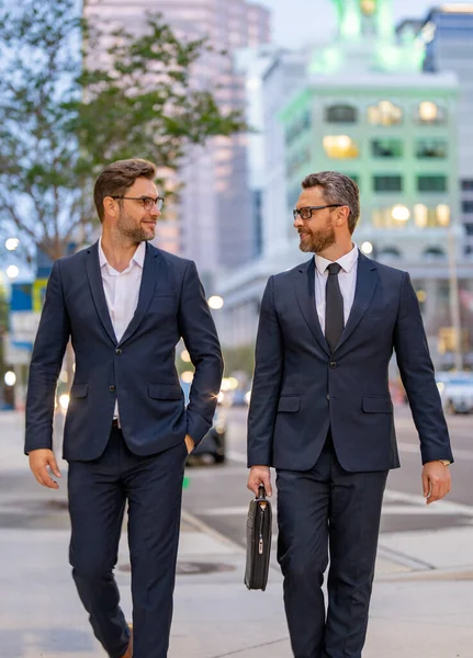 Businessmen communicating at meeting. Two businessmen discussing outdoor during business meeting. Businessmen talking. Business partners walking outdoor. 40s businessman walking by street