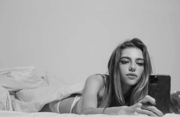 年轻的性感女人在床上用智能手机 — 图库照片