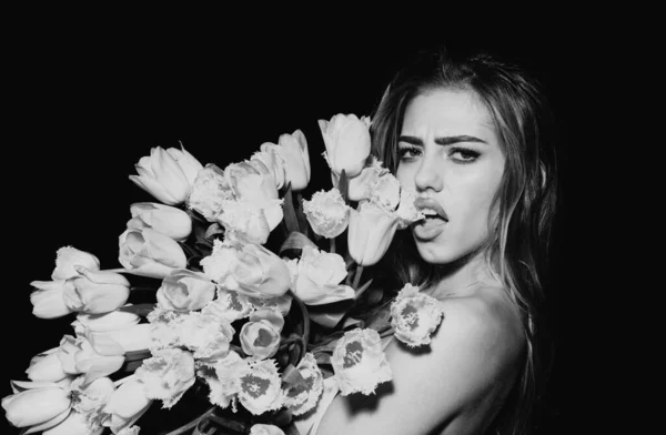 一个带着花的年轻女人美丽的姑娘把一束郁金香束在黑色的背景上 带着性感的表情粘在舌头上 — 图库照片