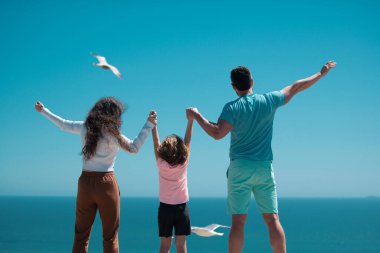 Sahildeki aile manzarası. Yaz tatilindeki insanlar. Baba, anne ve çocuk mavi denize karşı el ele tutuşuyorlar. Tatil seyahati kavramı