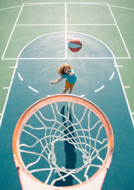 Basketbol formalı çocuk basket sahasında basket topuyla zıplıyor.