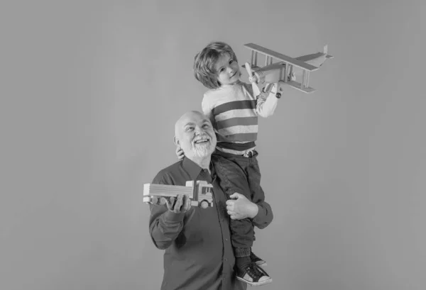 おもちゃの飛行機や木製のトラックと若い孫と古い祖父のピギーバック 男系の祖父 — ストック写真