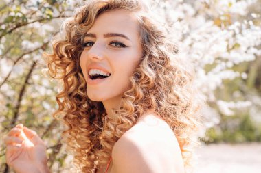 Bahar kıvırcık kız gülümsüyor. Orchard Blooming çiçekler şehvetli sarışın. Bahar gün kavramı. İyi günler