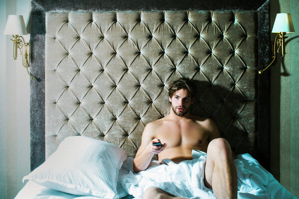 Carefree guy enjoying morning. Shirtless man in bedroom. Handsome man in underwear sitting on bed