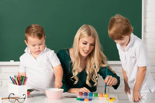 母と2人の息子が一緒に絵を描く ママは子供の男の子を助ける 学校でクラスの子供を助ける教師の家庭教師 — ストック写真