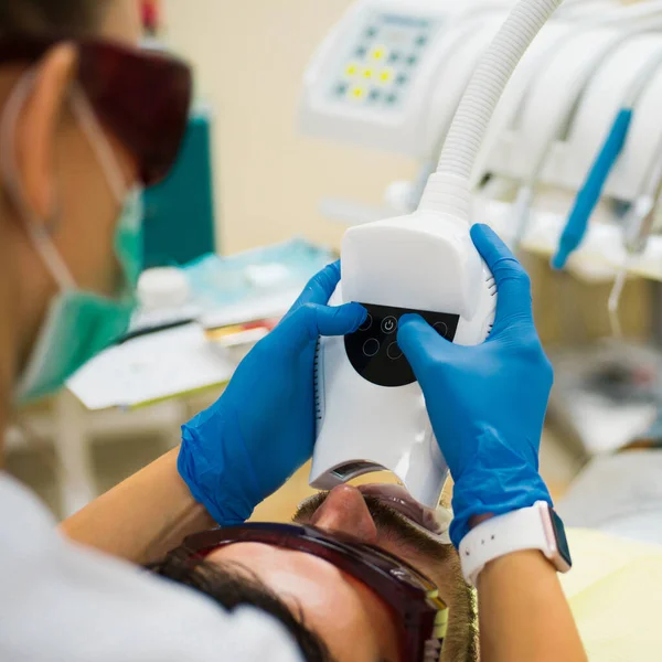 美丽的男人微笑与健康的牙齿美白 患者在牙科诊所用紫外线进行牙科检查 现代牙科诊所用镜子检查病人牙齿的女牙医 — 图库照片