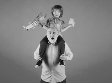 Grandson child and grandfather piggyback ride with plane and wooden toy truck. Men generation granddad and grandchild