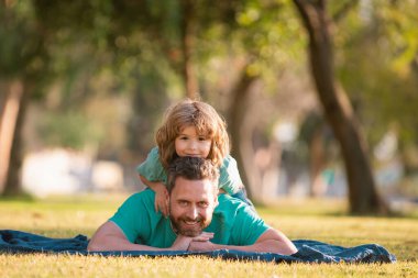 Baba ve oğul çimenlerde uzanıp parkta doğada dinleniyorlar. Çocukluk ve ebeveynlik kavramı