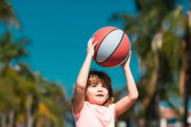 Küçük çocuk basket topuyla basketbol oynuyor. Arka planda basket topu olan çocuk, neşeli ve keyifli.