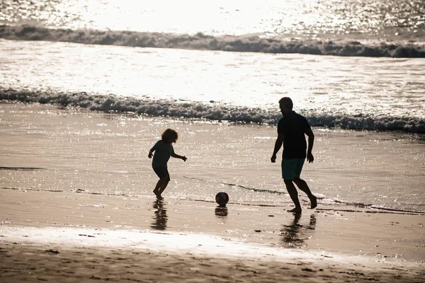 父と息子は夏休みにビーチでサッカーやサッカーをします 父と子供は屋外で楽しんでいます 夏の日に遊んでいる子供の男の子とパパ 日没のシルエット — ストック写真