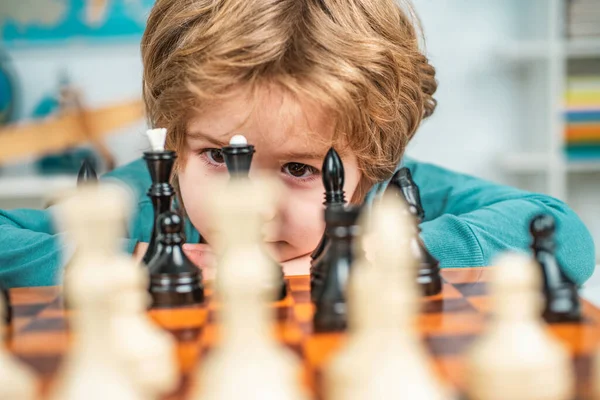 Cute little boy playing chess. Little clever boy thinking about chess. Concentrated little boy sitting at the table and playing chess. Portrait close up