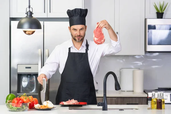 厨师成熟的人在厨房里穿围裙 一个英俊的男人在厨房里做饭 那家伙做了好吃的饭 男人在厨房里吃肉和蔬菜 厨房围裙休闲人的画像 — 图库照片
