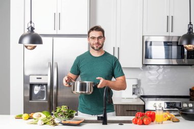 Aşçı adam mutfakta tencerede yemek pişiriyor. Gurme yemeği hazırlama süreci. Adam evde yemek pişiriyor, esrar kullanıyor. Şef yemek pişiriyor. Yakışıklı aşçı aşçı konsepti