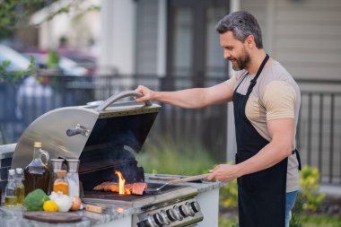 İspanyol adam arka bahçede barbekü pişiriyor. Şef barbekü hazırlıyor. Barbekü şefi. Önlüklü bir adam leziz ızgara ızgara yemek, bbq eti hazırlıyor. Izgara ve barbekü.
