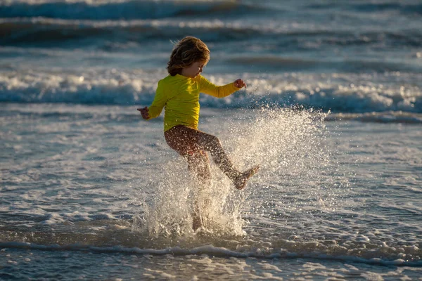 晴れた夏の日には波の海の近くの湿った海岸で走っている屈託のない少年を追放した 海に子供が飛び散った 子供は海の水のドロップで遊ぶ 小さな子供は水で遊んでスプラッシュを作る 子供は楽しい — ストック写真
