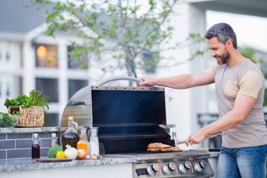 İspanyol adam arka bahçede barbekü pişiriyor. Şef barbekü hazırlıyor. Barbekü şefi. Barbekü hazırlayan yakışıklı adam, bbq eti. Izgara ve barbekü.