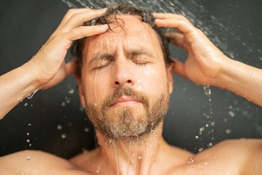 Milenyum adamı banyoda saç yıkıyor. Küvette banyo yapan adam. Yüzü duşta köpüklü. Banyo yapan adam duş alıyor. Yakından duş alan adam. Duş konsepti. İnsan duşta su altındadır.