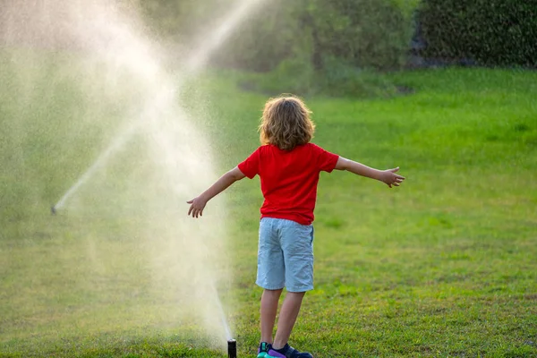 子供たちは水のホース 庭のスプリンクラー散水草で遊ぶ 子供のための夏の庭屋外の楽しみ 暑い夏の日に男の子が水を撒く 裏庭に子供の散水植物や草 — ストック写真