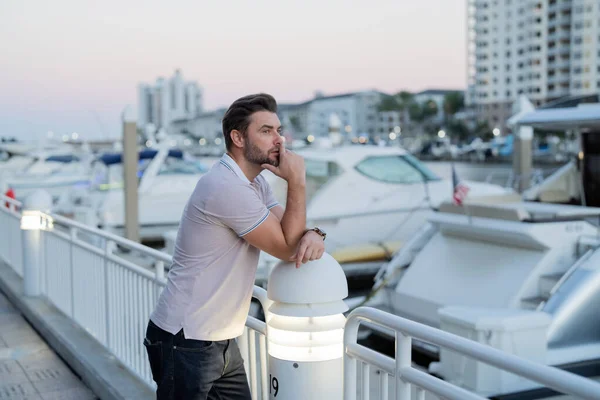 stock image Rich businessman dreaming and thinking near the yacht. Fashion male posing on the street background. Urban style. Young man walk through the city. Wealthy businessman posing next to office building