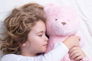 Çocuk tatlı rüyalar görüyor. Çocuk oyuncak ayıyla yatakta uyuyor, kestiriyor. Tatlı çocuk uyuyor.