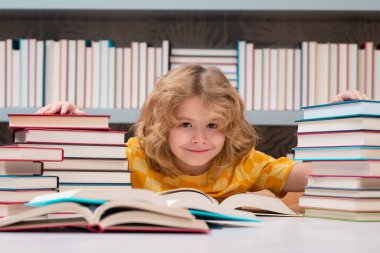 Küçük öğrenci kitap okuyor. Öğrenci çocuk okulda kitap okuyordu. Çocuk ödev yapıyor, kütüphanede, kitapların yanında oturuyor.