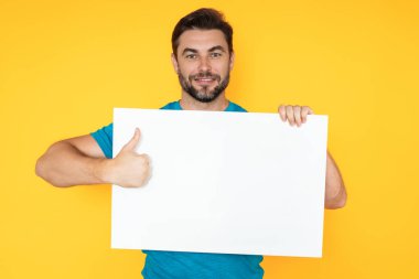 Stüdyo arka planında boş afişi olan bir adam. Elinde boş bir poster tutan adamın portresi. Boş afiş gösteren bir adam işaret ediyor. Erkek panosu, reklam panosu ya da panosu