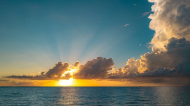 Gün batımı deniz manzarası. Sakin dalgalarla renkli sahil gündoğumu. Doğa deniz göğü. Mavi gökyüzüne ve denize karşı farklı renkte bulutlarla gün doğumu. Altından dramatik gökyüzü manzaralı deniz üzerinde gün batımı